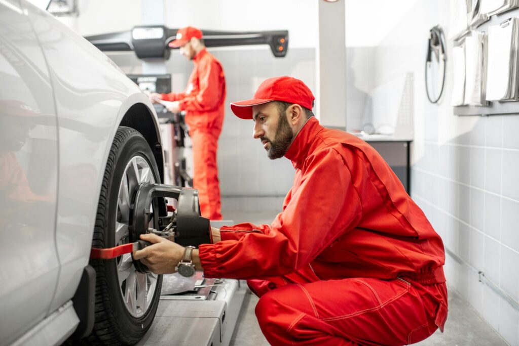 Embark on a smooth journey down the road with vehicle alignment from HiTech Automotive Auto mechanics making wheel alignment at the car service